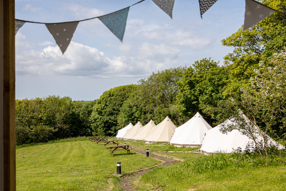 six bell tents in a line alongside wooden benches